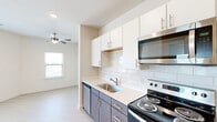 Located at 2700 E Howard Lane in Manor, TX, this efficiently designed one-bedroom, one-bathroom unit offers a clean, contemporary aesthetic throughout its single-floor layout. Light wood-style flooring runs continuously through the space, complementing the bright, neutral color palette that enhances the sense of openness.

The kitchen is a standout feature, outfitted with two-tone cabinetry — white upper cabinets paired with wood-finish lower cabinets — and a classic white subway tile backsplash. Stainless steel appliances include a refrigerator, electric range, microwave, and dishwasher, all set against light quartz countertops with an undermount sink. Recessed lighting illuminates the workspace effectively.

The living area flows naturally from the kitchen and benefits from natural light through a window, along with a ceiling fan for added comfort. The bedroom is a well-proportioned retreat featuring a ceiling fan, a window with outdoor views, and a sliding-door closet with built-in shelving for organized storage.

The bathroom is clean and functional, featuring a full soaking tub and shower combination enclosed with white tile surround, complemented by a wood-finish overhead cabinet for additional storage. The unit presents a cohesive, modern design well-suited for comfortable everyday living.