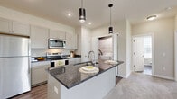Located in Lewis Center, Ohio, this well-appointed one-bedroom, one-bathroom residence offers a thoughtfully designed single-floor layout. The open-concept kitchen and living area serves as the heart of the home, showcasing dark granite countertops, crisp white shaker cabinetry, and a full suite of stainless steel appliances including a refrigerator, electric range, and over-the-range microwave. A central kitchen island with an undermount sink and pendant lighting adds both function and style, while wood-look flooring flows throughout the main living and kitchen areas. The spacious bedroom features vaulted ceilings that lend an airy, open feel, plush carpeting, a ceiling fan, and multiple windows that invite an abundance of natural light and outdoor views. Two closets provide generous storage, including a walk-in closet with wire shelving. The bathroom is finished with wood-look flooring, a tub/shower combination, and a window for natural light. A dedicated in-unit laundry room adds everyday convenience, and a private balcony offers an outdoor retreat. Neutral tones and clean finishes throughout create a cohesive, modern ambiance well-suited to comfortable living.