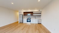 Located at 23 North Broadway Street in Tacoma, Washington, this modern one-bedroom, one-bathroom residence offers a thoughtfully designed layout with clean, contemporary finishes throughout. Light-toned hardwood flooring runs continuously across the entire space, lending a sense of warmth and cohesion.

The open-concept kitchen and living area serves as the heart of the home. The kitchen is outfitted with stainless steel appliances — including a refrigerator, electric range, built-in microwave, and dishwasher — complemented by white lower cabinetry, rich dark-wood upper cabinets, open shelving, and a tile backsplash. Recessed lighting illuminates the space efficiently. The adjacent living area is bathed in natural light through expansive floor-to-ceiling windows that frame sweeping views of Tacoma's urban skyline.

The bedroom is a quiet, well-proportioned retreat featuring a large window with city views and clean white walls. A dedicated closet offers wire shelving and generous storage capacity. The bathroom presents a minimalist aesthetic with a soaking tub and shower combination, a wide vanity with an integrated sink, and a large mirror.

A bright hallway with recessed lighting and a sliding-door closet connects the rooms seamlessly, completing this well-appointed urban residence.