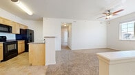 This single-floor, 2-bedroom, 1-bathroom residence offers a thoughtfully organized layout across a comfortable footprint. The open-concept living area features warm beige carpet and flows directly into the kitchen, which is finished with light oak cabinetry, dark countertops, tile flooring, and a full suite of black appliances including a range, refrigerator, microwave, and dishwasher. A breakfast bar peninsula separates the kitchen from the living space, and a ceiling fan overhead adds to the room's functionality. Natural light fills both bedrooms through large windows, each equipped with ceiling fans and plush carpeting. The spacious primary bedroom includes direct access to a generous walk-in closet outfitted with double-tiered wire shelving, as well as a view into the hallway leading to the bathroom. The second bedroom is bright and well-sized, also benefiting from ample natural light and neighborhood views. The bathroom features tile flooring, an oak vanity with a dark countertop, a large mirror, and clean, neutral finishes. A connecting hallway ties together the bedroom wing and includes additional closet storage. Throughout the home, a consistent palette of white walls, warm wood tones, and neutral flooring creates a cohesive and welcoming atmosphere.