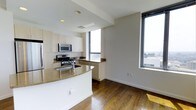 Unit 28D is a well-appointed two-bedroom, two-bathroom residence situated on a high floor, offering sweeping city views through generous floor-to-ceiling windows. The open-concept layout maximizes the available space, creating a seamless flow between the kitchen and living areas.

The kitchen is a standout feature, equipped with stainless steel appliances, including a gas range and built-in microwave. Granite countertops extend across the workspace and wrap around a curved peninsula, providing additional seating and prep space. Light-toned cabinetry offers ample storage, while the kitchen's position adjacent to large windows ensures excellent natural light throughout the day.

Rich hardwood flooring runs throughout the main living area, adding warmth and continuity to the space. The living area benefits directly from the corner window placement, allowing for abundant natural light and panoramic views of the surrounding cityscape.

The unit's single-floor layout provides straightforward, accessible living with two bedrooms and two full bathrooms. The overall ambiance is modern and functional, combining practical finishes with elevated views, making it a well-rounded urban residence suited for contemporary living.