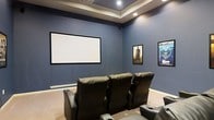 This dedicated home theater is designed to deliver an authentic cinema experience within a private setting. The room is anchored by a large, wall-mounted projection screen that serves as the focal point, providing an expansive viewing surface ideal for movies and entertainment. Deep blue walls enhance the immersive atmosphere, minimizing light reflection and adding a dramatic, theater-like ambiance throughout the space.

Overhead, a tray ceiling with integrated recessed lighting adds architectural depth and a refined aesthetic touch, while allowing for adjustable illumination to suit any viewing environment. The flooring is finished in neutral carpet, contributing to the room's acoustics and overall comfort.

Seating is provided by a tiered arrangement of premium black leather recliner chairs, each equipped with armrests and cup holders, ensuring maximum comfort during extended viewing sessions. Classic movie posters adorn the walls, reinforcing the cinematic theme and adding a personal, curated character to the room.

The thoughtful layout and design elements — from the acoustically friendly surfaces to the carefully positioned seating — make this home theater a standout entertainment space, well-suited for an elevated and immersive movie-watching experience.
