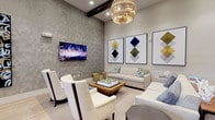 This well-appointed single-floor amenity center offers a thoughtfully designed collection of social and functional spaces, each finished with contemporary décor and quality materials throughout. The welcoming entry corridor features multiple glass doors, framed artwork, and light wood-style flooring that flows through the entirety of the facility.

The main lounge area is anchored by a textured accent wall, a wall-mounted flat-screen TV, and elegant seating arrangements including a neutral sofa and white accent chairs gathered around a wood coffee table. A statement woven chandelier and exposed wood ceiling beam add architectural character overhead. An adjacent relaxed seating nook with leather club chairs, patterned drapery, and eclectic wall art provides a more intimate retreat.

The game room is a standout feature, offering a billiards table, shuffleboard, bar-height seating, and a mounted television — all beneath industrial-style pendant lighting and light wood flooring. A dedicated card room with a round gaming table, upholstered chairs, and patterned curtains offers a quieter space for leisure.

The business suite includes a large wood conference table, task seating, a private desk station, bold dark-green accent wall, and Edison bulb chandelier. The full catering kitchen is sleek and functional, featuring white shaker cabinetry, quartz countertops, stainless steel appliances, a light blue tile backsplash, and decorative metallic wall art.