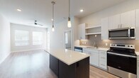 This single-floor residence showcases a contemporary design with a thoughtful, open layout. The kitchen serves as a central highlight, featuring a large dark-based island topped with a crisp white countertop and illuminated by stylish pendant lighting. White flat-front cabinetry extends to the ceiling, complemented by a neutral tile backsplash and a full suite of stainless steel appliances, including a side-by-side refrigerator, electric range, built-in microwave, and dishwasher.

The kitchen flows seamlessly into an open living area finished with light-toned hardwood-style flooring. Multiple windows fitted with horizontal blinds fill the space with natural light, while a ceiling fan adds comfort overhead. A door leads to a private balcony offering views of the surrounding community.

The bedrooms are carpeted for warmth and comfort, each equipped with ceiling fans and windows that bring in ample daylight. Closet access is conveniently situated within each room. The bathroom is clean and well-appointed, featuring a white vanity with brushed nickel hardware, a framed mirror, and hardwood-style flooring. Grab bars provide added accessibility. Throughout, neutral tones and modern finishes create a cohesive, move-in-ready aesthetic.
