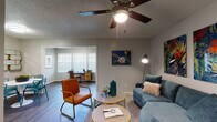 Located at 6016 Barton Hills Dr in Fort Worth, Texas, this single-story home offers a thoughtfully designed layout that balances comfort and functionality. The living area features dark hardwood-style flooring, neutral gray walls, and a ceiling fan, creating a welcoming atmosphere. A pass-through opening connects the living space to an adjacent dining area, which accommodates a round table and chairs beneath its own ceiling light. The open flow continues into a dedicated space suitable for a home office, framed by bright windows with slatted blinds that invite natural light. The kitchen is well-equipped with white cabinetry, sleek hardware, a mosaic tile backsplash, black appliances including a range and refrigerator, and light countertops. The bathroom features a full tub-shower combination with white tile surround, a vanity with speckled countertop, and hardwood-style flooring. The bedroom is a calm retreat with carpeted flooring, a ceiling fan, and a window overlooking the outdoors. A dedicated laundry area with utility hookups adds convenience. Throughout the home, textured ceilings and consistent neutral tones create a cohesive and practical living environment suited for everyday life in the Fort Worth area.