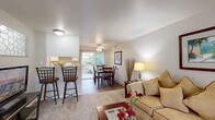 This single-floor residence offers a thoughtfully arranged layout comprising four bedrooms, one full bathroom, and a combined living, dining, and kitchen area. The open-concept main living space features plush carpeting in the living room, which flows seamlessly into the dining area and kitchen. The living room is bright and welcoming, with neutral-toned walls that complement the warm, natural light filtering through large windows and a sliding glass door. A ceiling fan adds comfort to the dining area, which connects directly to the kitchen. The kitchen is well-equipped with white cabinetry, laminate countertops, a full-size electric range, refrigerator, and durable wood-look flooring that continues into the dining and laundry areas. The bedrooms are carpeted and receive natural light from exterior-facing windows, offering a quiet and restful atmosphere. The primary bedroom provides a comfortable amount of space for furnishings. The shared bathroom features a combined tub-shower, a white vanity with laminate countertop, and wood-look flooring. A dedicated laundry area includes a full-size washer and houses the water heater, providing convenient in-unit utility access. Overall, this residence presents a clean, functional, and efficiently organized living environment.