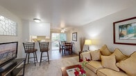 This single-floor residence offers a thoughtfully arranged layout comprising four bedrooms, one full bathroom, and a combined living, dining, and kitchen area. The open-concept main living space features plush carpeting in the living room, which flows seamlessly into the dining area and kitchen. The living room is bright and welcoming, with neutral-toned walls that complement the warm, natural light filtering through large windows and a sliding glass door. A ceiling fan adds comfort to the dining area, which connects directly to the kitchen. The kitchen is well-equipped with white cabinetry, laminate countertops, a full-size electric range, refrigerator, and durable wood-look flooring that continues into the dining and laundry areas. The bedrooms are carpeted and receive natural light from exterior-facing windows, offering a quiet and restful atmosphere. The primary bedroom provides a comfortable amount of space for furnishings. The shared bathroom features a combined tub-shower, a white vanity with laminate countertop, and wood-look flooring. A dedicated laundry area includes a full-size washer and houses the water heater, providing convenient in-unit utility access. Overall, this residence presents a clean, functional, and efficiently organized living environment.