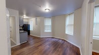 This efficiently designed one-bedroom, one-bathroom unit offers a well-organized single-floor layout with rich, dark hardwood flooring that runs throughout the entire space, creating a warm and cohesive feel. The open living area is brightened by multiple windows fitted with blinds, allowing ample natural light to fill the room. The curved wall in the living area adds a distinctive architectural touch, giving the space a unique character uncommon in similarly sized units.

The kitchen is thoughtfully appointed with gray shaker-style cabinetry, dark granite countertops, and black appliances including a full-size refrigerator and an electric range with an overhead exhaust fan. A window in the kitchen provides additional natural light, enhancing the functional workspace.

The bedroom offers a comfortable footprint with a window overlooking the exterior, a closet with paneled doors, and the same consistent hardwood flooring found throughout. It connects conveniently back to the main living and kitchen areas.

The bathroom is clean and modern, featuring large-format neutral tile surrounding a full soaking tub and shower combination with a built-in niche, a white vanity, and chrome and brushed gold fixtures that add a refined finishing touch. Overall, the space is well-maintained and move-in ready.