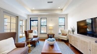 Located at 1106 Euclid Ave in Charlotte, NC, this thoughtfully designed single-floor space offers a cohesive layout comprising a living room, dining room, and connecting hallway. The living room is a standout feature, showcasing a tray ceiling with recessed lighting, rich hardwood floors, and multiple black-framed windows that invite generous natural light and views of an outdoor terrace. The room's open, airy feel is complemented by a neutral color palette and a rattan media console that adds warmth and texture. A hallway connects the spaces seamlessly, featuring white cabinetry, dark countertops, a coffee station, and elegant French doors with glass panes that lead into adjacent areas, enhancing the sense of openness. The dining room exudes a refined ambiance, anchored by a dramatic dark wood pedestal table surrounded by upholstered arm chairs. A tray ceiling mirrors the living room's architectural detail, while wall sconces and an overhead chandelier provide warm, layered lighting. A large-scale artwork adds a sophisticated focal point, and a black-framed window allows natural light to filter in. Throughout, the consistent use of hardwood flooring, tray ceilings, and crisp white walls creates a cohesive, polished aesthetic.