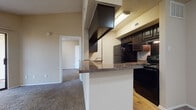 This single-floor residential unit offers a practical and cohesive layout designed for comfortable everyday living. The kitchen serves as a central feature, showcasing dark espresso-toned cabinetry, granite-style countertops, and black appliances including a refrigerator, electric range, and built-in microwave. A peninsula with a raised breakfast bar visually connects the kitchen to the adjoining living area, creating an open, pass-through feel. Warm hardwood-style flooring runs through the kitchen, while plush carpet extends throughout the living spaces, adding comfort underfoot. The living area is generously proportioned, with neutral beige walls, a textured ceiling, and a pass-through opening that frames the kitchen beyond. A sliding glass door in the bedroom fills the space with natural light and provides direct access to an outdoor patio area, with vertical blinds offering privacy when desired. The bedroom itself is well-sized with soft carpeting and ample wall space. The bathroom is cleanly appointed with a full tub and shower combination framed in white tile, dark wood cabinetry with matching countertops, a vanity mirror, and hardwood-style flooring that ties back to the kitchen aesthetic. Overall, the unit presents a consistent, neutral palette with coordinated finishes throughout.