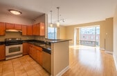 This single-floor residence is designed with an open-concept layout that seamlessly connects the kitchen and living area. The kitchen is a functional and well-appointed space, featuring rich wood cabinetry, dark granite countertops, and an electric range with an overhead ventilation hood. A peninsula with a built-in sink and additional counter space extends into the living area, above which two pendant lights hang, providing focused illumination. Stainless steel appliances complement the cabinetry. The living area features warm bamboo hardwood flooring and receives generous natural light through large windows, which also frame views of the surrounding urban landscape. A sliding glass door leads to an outdoor area, further enhancing the connection to the exterior.

The bedrooms are carpeted and neutrally painted, offering a calm and versatile environment. The bathroom includes a single-sink vanity with wood cabinetry, a large wall mirror, tile flooring, and a full bathtub and shower combination. The overall design of the space is clean and modern, with neutral tones throughout, white trim, and an efficient floor plan that maximizes usability across each area.