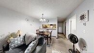 Located at 1279 Coffeen Street in Watertown, New York, this single-floor residence offers a practical and well-organized layout designed for comfortable everyday living. The living room features neutral-toned carpet, light gray walls, and a large window dressed with sheer curtains that allow natural light to fill the space. A baseboard heating unit runs along the wall, providing efficient warmth. Adjacent to the living area, the dining space is defined by a pendant chandelier overhead and connects seamlessly to the kitchen via a pass-through counter opening, creating an open and communicative flow between rooms. The kitchen is equipped with cream-toned cabinetry, ample counter space, a stainless steel range, dishwasher, and tile flooring, offering a fully functional cooking environment. The bedroom is a comfortable retreat featuring multiple windows that bring in natural light, soft carpeting, and a textured ceiling. The bathroom includes a vanity with under-sink cabinetry, a wall-mounted mirror with overhead lighting, and tile flooring, with a shower-tub combination enclosed by a curtain. Throughout the residence, a consistent neutral color palette and straightforward design create a cohesive and inviting atmosphere.