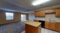 This single-floor residence offers a thoughtfully designed open-concept layout that seamlessly connects the kitchen and living area. The kitchen is well-appointed with warm honey-toned wood cabinetry, a full suite of black appliances including a refrigerator with ice maker, electric range, built-in microwave, and dishwasher, complemented by a central island topped with granite counters and light tile flooring. Crown molding adds a refined touch throughout the main living spaces.

The living area features a distinctive tray ceiling that adds architectural depth, soft carpeting underfoot, and sliding glass door access to a private balcony, flooding the space with natural light. A secondary living or flex room also provides balcony access through a glass door and includes a window for additional natural light.

The bedrooms are carpeted and generously proportioned, with windows that invite natural light. The primary bedroom includes a walk-in closet with built-in shelving and rod storage, as well as direct access to a dedicated laundry area with a washer and dryer. The bathroom features tile flooring, a full soaking tub with a floor-to-ceiling tile surround, and a vanity. Textured ceilings and consistent neutral-toned walls are present throughout the entire space.