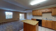 This single-floor residence offers a thoughtfully designed open-concept layout that seamlessly connects the kitchen and living area. The kitchen is well-appointed with warm honey-toned wood cabinetry, a full suite of black appliances including a refrigerator with ice maker, electric range, built-in microwave, and dishwasher, complemented by a central island topped with granite counters and light tile flooring. Crown molding adds a refined touch throughout the main living spaces.

The living area features a distinctive tray ceiling that adds architectural depth, soft carpeting underfoot, and sliding glass door access to a private balcony, flooding the space with natural light. A secondary living or flex room also provides balcony access through a glass door and includes a window for additional natural light.

The bedrooms are carpeted and generously proportioned, with windows that invite natural light. The primary bedroom includes a walk-in closet with built-in shelving and rod storage, as well as direct access to a dedicated laundry area with a washer and dryer. The bathroom features tile flooring, a full soaking tub with a floor-to-ceiling tile surround, and a vanity. Textured ceilings and consistent neutral-toned walls are present throughout the entire space.