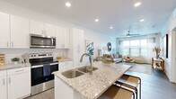 This single-floor residence in Midvale, Utah, offers a thoughtfully designed open-concept layout that seamlessly connects the kitchen, dining, and living areas. The kitchen is a standout feature, outfitted with crisp white cabinetry, a subway tile backsplash, stainless steel appliances including a refrigerator, range, microwave, and dishwasher, and a granite-topped island with a double stainless steel sink and bar seating — ideal for both cooking and casual dining. Wood-look flooring runs throughout the main living areas, adding warmth and continuity to the space. The living room is bright and welcoming, benefiting from large windows that invite generous natural light, and is finished with a ceiling fan. The bedroom continues the clean, modern aesthetic, featuring a ceiling fan, a large window dressed with blinds and drapes, and direct access to a walk-in closet with built-in shelving and hanging rods. The bathroom is finished with granite countertops, white cabinetry, and wood-look flooring, maintaining the cohesive design language found throughout the home. Recessed lighting throughout enhances the clean, contemporary feel of every room, making this a well-appointed and comfortable single-level home.