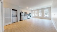 Located at 5000 Libbie Lake South Street in Richmond, Virginia, this single-floor unit offers a clean, contemporary design highlighted by light wood-style flooring and a neutral color palette throughout. The open layout connects the living area to the kitchen seamlessly, creating a spacious and functional environment.

The kitchen is well-appointed with white shaker-style cabinetry, light countertops, and a gray tile backsplash. Stainless steel appliances include a refrigerator, electric range, over-the-range microwave, and dishwasher, complemented by a black matte sink fixture. Ample upper and lower cabinet storage adds to the kitchen's practicality.

The living area is generously proportioned, benefiting from recessed lighting and large windows that allow natural light to fill the space. Two closet doors are visible at one end of the living area, offering convenient storage solutions.

An in-unit laundry closet with a stacked washer and dryer is tucked neatly behind a louvered door, providing added convenience. The bathroom features large-format tile flooring, a white vanity with storage, and a full tub-shower combination with clean white surroundings, maintaining the unit's consistently bright and modern aesthetic.