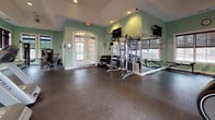Located at 400 Blake St in New Haven, CT, this well-appointed fitness center offers a spacious, single-floor layout designed to accommodate a comprehensive range of workout options. The room is finished with distinctive sage-green walls and dark rubberized flooring, creating a clean and energizing environment for exercise.

Large arched and rectangular windows line the walls, flooding the space with abundant natural light and offering views of the surrounding exterior. French-style glass doors provide additional brightness while offering easy access to and from the facility. Recessed ceiling lighting and track lighting supplement natural light throughout the day.

The cardio section is well-equipped with multiple treadmills, elliptical trainers, and stationary bikes, including recumbent models, arranged to take advantage of the natural light. A dedicated strength training area features a cable and pulley multi-station machine along with additional resistance equipment, providing options for a full-body workout. Exercise mats and supplementary fitness accessories are also available for stretching or floor-based training.

A ceiling fan provides airflow throughout the space, and ample open floor area ensures comfortable movement between equipment stations. The overall layout is thoughtfully organized, balancing cardio and strength zones to deliver a functional and inviting fitness experience.