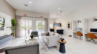 Located at 4150 Davie Road Ext in Hollywood, Florida, this single-story community amenity space offers a thoughtfully designed environment that blends modern aesthetics with practical functionality. The entrance welcomes visitors through floor-to-ceiling frameless glass doors, opening into a bright, open-plan interior finished with large-format white tile flooring throughout.

The central lounge area serves as the social heart of the space, featuring a sleek wall-mounted entertainment center, contemporary furnishings, and direct access to the outdoor pool area through expansive glass French doors framed with sheer drapery. Recessed lighting and a neutral color palette create a bright, airy atmosphere.

Adjacent to the lounge is a well-appointed kitchen with matte navy cabinetry, warm wood-toned backsplash, white quartz countertops, a peninsula with bar seating, pendant lighting, and a built-in beverage cooler — ideal for community gatherings. A glass-enclosed leasing and business office provides a transparent, professional workspace visible from the main lounge.

The fitness center is generously equipped with a full suite of cardio machines, including treadmills and ellipticals, as well as a comprehensive selection of strength equipment, free weights, and floor-to-ceiling mirrors. Wood-look flooring and recessed lighting complete the clean, functional aesthetic of this well-rounded amenity facility.