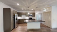 Located at 6004 Grandover Village Rd in Greensboro, NC, this single-floor residence offers a well-designed layout with modern finishes throughout. The kitchen serves as a focal point of the home, showcasing taupe shaker-style cabinetry, a white subway tile backsplash, dark granite countertops, and a full suite of stainless steel appliances including a French door refrigerator, electric range, microwave, and dishwasher. A large central island with a contrasting white base provides additional workspace and seating, while two elegant glass pendant lights add a refined touch overhead. Recessed lighting and wood-look plank flooring complete the kitchen's contemporary aesthetic. The open living area features durable wood-look flooring, a ceiling fan with lighting, and a neutral color palette that maximizes the sense of space. Bedrooms are finished with plush carpet, ceiling fans, and generous natural light. One bedroom includes built-in shelving with a curved architectural detail, adding both function and character. The bathrooms are well-appointed, with one featuring a double vanity with granite countertops and a walk-in shower, and another offering a single vanity with a soaking tub and shower combination. Stone-look tile flooring and chrome fixtures complete the bathrooms' clean, modern look.
