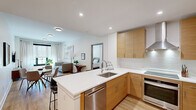 Located at 600 North Avenue in New Rochelle, NY, this thoughtfully designed 2-bedroom, 2-bathroom residence offers a clean, contemporary aesthetic throughout its single-floor layout. The open-concept kitchen and living area serves as the heart of the home, anchored by a large island with white quartz countertops and seating for multiple guests. Warm wood cabinetry, subway tile backsplash, stainless steel appliances — including a French door refrigerator and range with a ventilation hood — complete the well-equipped kitchen. Light hardwood flooring runs throughout, enhancing the bright, airy feel of the space. The living room features bold black-framed windows that invite abundant natural light, complemented by clean white walls that create a versatile backdrop. The spacious primary bedroom offers generous proportions, large windows with sheer drapery, and a serene atmosphere. Both bathrooms are finished with warm wood vanities, white quartz counters, large mirrors, and marble-patterned tile flooring. The primary bath includes a walk-in shower, while the second bath features a soaking tub and shower combination. A hallway and closet provide practical storage solutions, rounding out this well-planned and stylish residence.