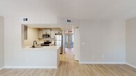 This well-designed single-floor residence offers a clean, modern aesthetic defined by neutral tones, light wood-style flooring, and bright white walls throughout. The open-concept layout connects the kitchen and living areas seamlessly, creating a spacious and airy feel. The kitchen is thoughtfully appointed with grey shaker-style cabinetry, white quartz countertops, a black matte sink faucet, and a full suite of stainless steel appliances including a refrigerator, electric range, microwave, and dishwasher. A peninsula counter with a breakfast bar overhang provides both additional prep space and a natural division between the kitchen and the adjacent dining or living area. The living space is generously proportioned, bathed in natural light, and features consistent light-toned flooring that extends throughout the unit. A hallway connects the main living areas to the private rooms, with a view toward what appears to be a carpeted bedroom at the far end. The bathroom showcases a grey vanity with quartz countertops, an undermount sink, black hardware accents, and a full tub-shower combo with white tile surround. Ceiling-mounted light fixtures, HVAC vents, and clean white baseboards complete the polished, move-in-ready presentation of this thoughtfully updated space.