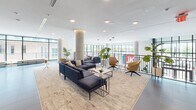 Located at 916 West St in Charlottesville, VA, this contemporary single-floor amenity space is designed with a polished, modern aesthetic that balances social and productive environments. The layout encompasses several distinct zones that flow seamlessly into one another across large-format tile flooring throughout.

The main lounge area features exposed concrete columns, floor-to-ceiling windows, and an abundance of natural light, furnished with navy sectional sofas, woven area rugs, and accent chairs that create a welcoming, collaborative atmosphere. Adjacent to the lounge, a game and entertainment room showcases a striking slatted wood ceiling detail, a wall-mounted television above a sleek linear fireplace, a pool table, and direct access to an outdoor terrace through expansive glass doors.

The kitchen and bar area is anchored by long white islands lined with black counter-height chairs, pendant lighting overhead, and a café-style station along the back wall with open shelving and decorative tile accents. A reception and lobby area near the entrance provides mounted screens, built-in cabinetry, and comfortable seating for arrivals.

An upper mezzanine-style overlook connects to dedicated coworking nooks and glass-walled private rooms, offering quieter work settings. Throughout, curated artwork, indoor plants, and consistent modern finishes reinforce a cohesive, upscale ambiance.