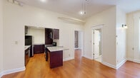 Located at 20 St. Louis Place in Buffalo, NY, this efficiently designed single-floor unit offers a well-organized layout that makes excellent use of its cozy footprint. Warm hardwood flooring runs throughout the main living areas, complementing the neutral cream-toned walls and creating a cohesive, inviting atmosphere.

The kitchen is a standout feature, showcasing rich dark cabinetry paired with granite countertops and stainless steel appliances, including a refrigerator, gas range, and built-in microwave. A peninsula-style island provides additional prep space and a natural dividing point between the kitchen and living areas. Notably, a stacked washer and dryer unit is tucked conveniently within the kitchen space, adding significant practical value.

The living room is bright and open, benefiting from natural light through a double-hung window framed in classic white trim. A striking exposed brick accent wall lends industrial character and historic charm to the space, while a ceiling fan adds comfort. High ceilings further enhance the sense of openness throughout.

The bathroom features light tile flooring, a glass-enclosed shower, and a frosted glass block window that allows natural light while maintaining privacy. Dark cabinetry above provides useful storage. The overall ambiance of this Buffalo unit blends historic architectural details with modern, functional finishes.