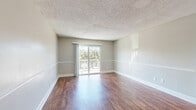 Located at 2320 S Conway Rd in Orlando, FL, this single-story home offers four bedrooms and two bathrooms across a well-organized floor plan. Rich hardwood-style flooring flows throughout the main living areas, complemented by neutral gray walls and crisp white baseboards that create a clean, consistent aesthetic. The living room is bright and spacious, featuring sliding glass doors that open to a private patio with outdoor views, allowing natural light to fill the space. Adjacent to the living room, the dining area features a pendant light fixture and a pass-through window connecting directly to the kitchen, enhancing the open feel between spaces. The kitchen is well-appointed with dark espresso cabinetry, granite countertops, a mosaic tile backsplash, and black appliances including a range and refrigerator. Each of the four bedrooms is finished with plush carpet and neutral tones, offering a comfortable retreat. The primary bedroom includes a walk-in closet with built-in shelving, providing ample storage. Five closets total are distributed throughout the home. The two bathrooms are clean and functional, with one featuring a tiled tub-shower combination. Textured ceilings are present throughout, adding a classic character to the home's overall design.