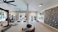 Located at 1351 East Woodlawn Road in Charlotte, NC, this fitness center offers a comprehensive exercise environment across a single, open floor. The space is thoughtfully designed to accommodate a wide range of workout styles, from cardio and strength training to functional fitness and climbing.

The main exercise area features multiple treadmills and elliptical machines by Matrix, lined along large black-framed windows that flood the room with natural light and offer views of the surrounding greenery. Overhead, large ceiling fans ensure comfortable airflow throughout the space. A centrally positioned functional training rig supports TRX suspension systems and battle ropes, while a tire and sled provide options for high-intensity conditioning work. A dedicated rack holds kettlebells, medicine balls, and free weights for strength-focused routines.

A standout feature is the textured climbing wall, branded as the "Freedom Climber," which adds a unique vertical training element to the space. The flooring transitions between durable rubber and carpet zones, delineating different workout areas effectively.

A separate, glass-partitioned studio room offers a more private setting for yoga, stretching, or small group workouts. Adjacent to the studio, a built-in cubby and bench area provides a convenient space for storing personal belongings. A wall-mounted TV and colorful geometric wall art add visual energy to the overall design, creating a motivating and modern atmosphere.