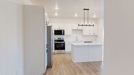 Located on 25th St S in Fargo, North Dakota, this well-designed 2-bedroom, 1-bathroom residence offers a thoughtful layout with modern finishes throughout its single floor. The open-concept kitchen and living area serves as the heart of the home, where warm hardwood-style flooring flows seamlessly underfoot. The kitchen is a standout feature, boasting crisp white shaker cabinetry, a large center island with quartz countertops, a full suite of stainless steel appliances, and an elegant pendant chandelier that anchors the space. The adjacent living room benefits from a sliding glass door that invites natural light and provides outdoor views. Both bedrooms are carpeted for comfort, with one featuring a spacious walk-in closet with wire shelving and another with a double-door closet, offering generous storage. The bathroom is finished with warm hardwood-style flooring, white cabinetry with matte black hardware, and a clean, contemporary vanity. Crisp white walls, recessed lighting, and black hardware accents throughout lend the space a cohesive, modern aesthetic. This residence combines functional design with stylish details for comfortable everyday living.