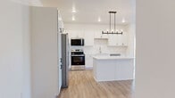 Located on 25th St S in Fargo, North Dakota, this well-designed 2-bedroom, 1-bathroom residence offers a thoughtful layout with modern finishes throughout its single floor. The open-concept kitchen and living area serves as the heart of the home, where warm hardwood-style flooring flows seamlessly underfoot. The kitchen is a standout feature, boasting crisp white shaker cabinetry, a large center island with quartz countertops, a full suite of stainless steel appliances, and an elegant pendant chandelier that anchors the space. The adjacent living room benefits from a sliding glass door that invites natural light and provides outdoor views. Both bedrooms are carpeted for comfort, with one featuring a spacious walk-in closet with wire shelving and another with a double-door closet, offering generous storage. The bathroom is finished with warm hardwood-style flooring, white cabinetry with matte black hardware, and a clean, contemporary vanity. Crisp white walls, recessed lighting, and black hardware accents throughout lend the space a cohesive, modern aesthetic. This residence combines functional design with stylish details for comfortable everyday living.