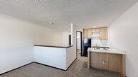 Located at 2440 NE 68th St in Gladstone, Missouri, this single-floor unit offers a practical and efficient layout designed to maximize every square foot of available space. The living area features neutral-toned carpet flooring, crisp white walls, and a textured ceiling, creating a clean and understated ambiance. A low half-wall partition separates the living area from the kitchen, offering a subtle sense of division while maintaining an open feel throughout the space.

The kitchen is well-appointed with light wood cabinetry providing ample storage, white quartz-style countertops, and a kitchen island that houses a four-coil electric cooktop — a functional centerpiece for meal preparation. A black refrigerator anchors one side of the kitchen, while a single-basin sink with a gold-toned faucet is neatly positioned along the back wall. Tile flooring in the kitchen area offers durability and easy maintenance.

The entry area features a bold black door paired with a window fitted with horizontal blinds, allowing for natural light while maintaining privacy. A wall-mounted HVAC unit provides climate control. The textured ceilings carry throughout the space, adding consistent character. Overall, the unit presents a straightforward, functional living environment suited for efficient everyday use.