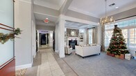 Located at 4430 N Holland Sylvania Rd in Toledo, Ohio, this single-story amenity facility offers a generous and thoughtfully designed layout across five distinct areas. The welcoming lounge area sets an elegant tone with coffered ceilings, decorative white columns, large windows that invite abundant natural light, and a stone-surround fireplace flanked by built-in shelving. Comfortable seating and soft carpeting create a warm, residential ambiance throughout this gathering space. A wide corridor with tray ceilings and tile flooring connects the various areas, adorned with decorative wall accents that add character to the transitional spaces. The private theater features tiered rows of plush black leather reclining seats, dark paneled walls with framed artwork, and a projection system — delivering an immersive cinematic experience. The expansive fitness center is outfitted with a comprehensive range of strength and cardio equipment, set beneath soaring vaulted ceilings with ceiling fans and large windows overlooking the exterior. A blue geometric carpet floor adds a modern touch to the workout space. An additional lounge or clubroom area features wood-look flooring, a large marble-topped island, modern track lighting, and glass-partitioned spaces ideal for gathering or meetings.