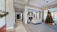 Located at 4430 N Holland Sylvania Rd in Toledo, Ohio, this single-story amenity facility offers a generous and thoughtfully designed layout across five distinct areas. The welcoming lounge area sets an elegant tone with coffered ceilings, decorative white columns, large windows that invite abundant natural light, and a stone-surround fireplace flanked by built-in shelving. Comfortable seating and soft carpeting create a warm, residential ambiance throughout this gathering space. A wide corridor with tray ceilings and tile flooring connects the various areas, adorned with decorative wall accents that add character to the transitional spaces. The private theater features tiered rows of plush black leather reclining seats, dark paneled walls with framed artwork, and a projection system — delivering an immersive cinematic experience. The expansive fitness center is outfitted with a comprehensive range of strength and cardio equipment, set beneath soaring vaulted ceilings with ceiling fans and large windows overlooking the exterior. A blue geometric carpet floor adds a modern touch to the workout space. An additional lounge or clubroom area features wood-look flooring, a large marble-topped island, modern track lighting, and glass-partitioned spaces ideal for gathering or meetings.