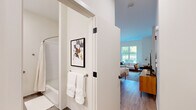 Located at 437 Cold Brook Dr in Sudbury, Massachusetts, this single-floor residence offers a thoughtfully designed open-concept layout that blends the living and sleeping areas into one cohesive, comfortable space. Light hardwood flooring runs throughout, providing a warm, cohesive foundation that ties the interiors together seamlessly.

The living area is anchored by a large picture window that frames lush outdoor greenery, flooding the room with natural light. The space comfortably accommodates a seating arrangement with a sofa, accent chairs, and a coffee table, making it well-suited for both relaxing and entertaining.

The sleeping area is generously proportioned, featuring ample room for a king-sized bed, a dedicated workspace with a desk and chair, a dresser, and a wall-mounted television. Additional windows continue to bring in natural light and garden views, enhancing the airy ambiance.

The bathroom is finished with neutral-toned tile flooring and clean white walls, and is equipped with accessibility features including sturdy grab bars and a tub-shower combination with a curved curtain rod. The overall design is practical and modern.

Throughout the unit, the aesthetic is clean and contemporary, with crisp white walls, recessed lighting, and a neutral palette that allows for flexible interior styling. The space offers a comfortable, well-lit environment with convenient access to Sudbury's surrounding amenities.