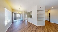 This single-floor residence offers a thoughtfully designed open-concept layout that seamlessly connects the main living and dining areas. Rich hardwood-style flooring runs throughout the common spaces, complemented by neutral-toned walls and an abundance of natural light streaming through large windows and sliding glass doors. A chandelier anchors the dining area, adding a refined touch to the space.

The kitchen is well-equipped with stainless steel appliances, including a refrigerator, range, and microwave, all set against crisp white cabinetry and light countertops. A subway tile backsplash and a tall pantry cabinet complete the functional and clean aesthetic. A pass-through counter connects the kitchen to the living area, enhancing the open feel. Built-in wall shelving near the hallway provides convenient display and storage space.

The bedrooms feature plush carpeting, ceiling fans, and multiple windows that invite natural light and exterior views. Each room offers a comfortable, airy atmosphere suited for rest and relaxation. The bathroom is finished with classic white cabinetry and stone-look countertops, maintaining the home's consistent, modern aesthetic. A hallway with hardwood-style flooring connects the private areas of the home, creating a cohesive and practical flow throughout.