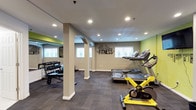 This fitness center offers a thoughtfully designed workout environment spread across a single level. The space features a clean, open layout with recessed lighting throughout, ensuring bright and consistent illumination across all exercise zones. Neutral gray walls are accented by vibrant green highlights, creating an energetic and motivating atmosphere, complemented by a bold "FITNESS" wall graphic that reinforces the space's purpose.

The cardio area is equipped with multiple treadmills and a cycling machine, positioned near windows that allow natural light to fill the room and provide a pleasant outlook during workouts. A dedicated free weights section features a full dumbbell rack alongside exercise mats, catering to strength training and flexibility exercises. Large mirrors line one wall, enhancing the sense of space and allowing users to monitor their form.

Structural archways and support columns add architectural character to the room, while carpet tile flooring provides comfort and durability underfoot. The space is well-ventilated and includes safety features such as sprinkler systems. Overall, this fitness center is designed to be both functional and inviting, offering residents or users a comprehensive facility for their daily health and wellness routines.