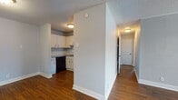 This single-floor residence offers a practical and comfortable layout designed for everyday living. The kitchen is well-equipped with white cabinetry, granite-style countertops, a subway tile backsplash, a built-in sink, and black appliances including an electric range, dishwasher, microwave, and refrigerator. Rich hardwood flooring runs throughout the main living and kitchen areas, adding warmth and cohesion to the space. A central hallway connects the key areas of the home, leading to the bedrooms and bathroom. The full bathroom features large-format dark tile surrounding a soaking tub and shower combo, paired with a granite-top vanity and hardwood flooring. The bedrooms are finished with soft carpeting and ceiling fans, and each benefits from natural light through windows with views of the surrounding greenery. One bedroom includes a spacious walk-in closet with built-in shelving and hanging rods for generous storage. The living areas are finished in a neutral gray palette with textured walls and ceilings, providing a clean and versatile backdrop. The dollhouse view confirms a compact yet efficient floor plan that maximizes the use of every square foot.