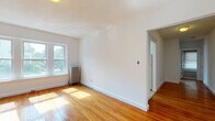 Located at 119 W Wyoming Ave in Melrose, MA, this single-floor unit offers a bright, well-organized layout with a clean, neutral aesthetic. Warm hardwood floors run continuously throughout the living areas, bedrooms, and hallway, lending a cohesive and inviting character to the entire space.

The living areas are generously proportioned, benefiting from multiple double-hung windows that invite abundant natural light and offer views of the surrounding neighborhood. Classic cast-iron radiators provide reliable heating in several rooms, a hallmark of traditional New England construction. White walls and clean trim work keep the interiors feeling fresh and airy.

The galley-style kitchen is efficiently arranged with wooden cabinetry, a gas range, refrigerator, and a stainless steel sink, with direct access to additional areas of the unit. The bathroom features classic white subway tile with a decorative border accent, a full soaking tub with an overhead shower, and a window for natural ventilation.

The bedrooms are well-sized, each with ample natural light. One bedroom includes two closets, one of which is a built-in rod closet, offering practical storage. A clean, straight hallway connects the rooms and adds to the efficient flow of the layout. Overall, this unit presents a timeless, functional design rooted in the character of its Melrose neighborhood setting.