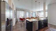 Located at 1145 Chambers Rd in Columbus, Ohio, this single-floor residence offers a thoughtfully designed layout with contemporary finishes and a warm, inviting ambiance. Rich hardwood-style flooring flows throughout the main living areas, grounding the open-concept design that seamlessly connects the kitchen, dining, and living spaces.

The kitchen serves as a central hub, featuring a large island with a sleek quartz countertop, deep single-basin sink, stainless steel appliances including a French door refrigerator, and bold dark cabinetry accented by white shaker-style upper cabinets with a classic subway tile backsplash. Pendant globe lights with brass accents hang above the island, adding a refined touch.

The living area is bright and welcoming, with large windows dressed in layered drapes that allow generous natural light. A defined seating area accommodates multiple conversation zones. The adjacent dining space features a glass door providing direct outdoor access, enhancing the connection to the outside.

Two well-appointed bedrooms offer comfortable, carpeted retreats with ample natural light. A stylishly finished bathroom features navy cabinetry, a quartz vanity top, and brass lighting fixtures. An entry corridor with wood-look flooring and recessed lighting completes the layout, creating a polished first impression upon arrival.