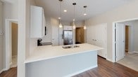 This well-appointed single-floor residence offers a clean, modern aesthetic with thoughtful finishes throughout. The open living and dining area is anchored by rich, dark hardwood flooring that flows seamlessly through the main living spaces, while large windows and a sliding glass door invite generous natural light and outdoor views, casting warm patterns across the floor.

The kitchen serves as a functional centerpiece, featuring crisp white shaker-style cabinetry, a classic subway tile backsplash, light stone countertops, and a spacious island with a built-in sink. Stainless steel appliances — including a refrigerator, range, and over-the-range microwave — complete the space, with stylish pendant lighting adding a polished touch overhead.

The bedrooms offer a comfortable retreat; the primary room features the same gleaming hardwood flooring, while additional bedrooms are finished with plush neutral carpet and well-placed windows that provide natural light. Warm taupe wall tones carry consistently throughout, lending the home a cohesive and calming character.

Two bathrooms round out the layout: one featuring a walk-in shower with built-in shelving, and another with a full soaking tub and shower combination, granite-accented vanity, and hardwood flooring. The overall design balances practicality with modern style, making this a move-in-ready space with lasting appeal.
