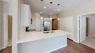 This well-appointed single-floor residence offers a clean, modern aesthetic with thoughtful finishes throughout. The open living and dining area is anchored by rich, dark hardwood flooring that flows seamlessly through the main living spaces, while large windows and a sliding glass door invite generous natural light and outdoor views, casting warm patterns across the floor.

The kitchen serves as a functional centerpiece, featuring crisp white shaker-style cabinetry, a classic subway tile backsplash, light stone countertops, and a spacious island with a built-in sink. Stainless steel appliances — including a refrigerator, range, and over-the-range microwave — complete the space, with stylish pendant lighting adding a polished touch overhead.

The bedrooms offer a comfortable retreat; the primary room features the same gleaming hardwood flooring, while additional bedrooms are finished with plush neutral carpet and well-placed windows that provide natural light. Warm taupe wall tones carry consistently throughout, lending the home a cohesive and calming character.

Two bathrooms round out the layout: one featuring a walk-in shower with built-in shelving, and another with a full soaking tub and shower combination, granite-accented vanity, and hardwood flooring. The overall design balances practicality with modern style, making this a move-in-ready space with lasting appeal.
