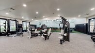 Located at 9727 Touchton Rd in Jacksonville, FL, this well-appointed fitness facility offers a comprehensive workout environment designed to accommodate a wide range of training styles. The single-floor layout is thoughtfully divided into distinct zones, each tailored to specific fitness activities.

The centerpiece of the facility is a spacious functional training area featuring artificial turf flooring accented by a bold red sprint/sled track. This zone is equipped with battle ropes, resistance sleds, agility hurdles, stability balls, a TRX suspension system, and a multi-functional rig — all set beneath soaring vaulted ceilings with exposed wood truss detailing and a clerestory row of windows that flood the space with natural light.

Adjacent to the turf zone, the strength training area houses a robust selection of selectorized machines, free weight benches, and cable systems, including an Instinct-branded functional trainer. Full-length mirrors and glass partitions visually expand the space and support proper form during workouts.

The cardio section is equipped with treadmills, ellipticals, stair climbers, air bikes, and rowing machines, all positioned alongside large dark-framed windows that bring in views of the surrounding outdoors. Recessed lighting throughout ensures consistent illumination across all workout zones, while neutral carpet tile flooring and a clean black-and-white color scheme contribute to a modern, professional aesthetic.