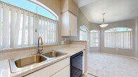 Located at 5151 E Guadalupe Rd in Phoenix, AZ, this single-story home offers five bedrooms and three bathrooms across a well-designed floor plan. The living room is a standout space, featuring soaring vaulted ceilings, a ceiling fan, a tiled fireplace with a classic white mantel, and multiple arched windows that flood the room with natural light. Soft carpeting and neutral tones create a warm, inviting atmosphere throughout.

The kitchen is efficiently laid out with white cabinetry, light stone-finish countertops, a double-basin stainless steel sink, a dishwasher, and a full-size refrigerator. Wood-look flooring anchors the kitchen, while arched windows continue the architectural theme, keeping the space bright. A pendant light fixture adds a subtle decorative touch.

The bedrooms are generously proportioned, carpeted, and well-lit with natural light from vertical-blind-covered windows. Several bedrooms include closets with built-in shelving for organized storage. The bathrooms are clean and functional, featuring tile-surround soaking tubs and vanities with stone-finish countertops and ample cabinetry. A hallway connects the bedrooms and bathrooms, providing a logical flow throughout the home.