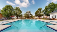 Located at 135 Reynoldsburg New Albany Rd S in Reynoldsburg, Ohio, this single-story property offers a notable outdoor amenity in the form of a large swimming pool. The pool area is a standout feature, showcasing clear, blue water within a spacious rectangular pool that is well-suited for both leisure and recreation. The surrounding pool deck provides ample room for lounge seating and relaxation, with multiple chairs and shaded umbrella stations positioned along the perimeter. A sturdy wrought iron fence encloses the entire pool area, offering both security and an open, airy aesthetic. Mature trees line the background, providing natural shade and a pleasant, park-like atmosphere that enhances the overall outdoor environment. The setting benefits from open sky exposure, allowing for abundant natural light throughout the day. The combination of the expansive pool, generous deck space, tree-lined surroundings, and well-maintained landscaping creates an inviting and functional outdoor space. This property is well-positioned within the Reynoldsburg community, offering convenient access to local amenities while maintaining a serene, residential feel.