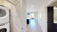 This well-appointed single-floor residence offers a thoughtfully designed layout across two bedrooms, one bathroom, an entrance, and a dedicated closet. Light-toned hardwood-style flooring flows seamlessly throughout the main living areas, complementing the clean, neutral palette of the walls and trim.

The open-concept kitchen and living area serves as the heart of the home. The kitchen is a standout feature, showcasing a striking two-tone design with navy lower cabinets, crisp white upper cabinetry, and light quartz countertops. A large center island with matching navy cabinetry provides generous prep space and is accented by a pair of matte black dome pendant lights suspended from brass fixtures. Stainless steel appliances, a subway tile backsplash, and a matte black faucet complete the contemporary aesthetic. A sliding glass door opens to an outdoor balcony, allowing natural light to pour into the living area.

The primary bedroom is generously sized, featuring large windows with views of the surrounding neighborhood and built-in shelving. The second bedroom offers plush carpeting and a closet with direct natural light from a side window. The bathroom is finished with a dark wood vanity, white quartz countertop, and a full tub-shower combination accented with matte black fixtures.