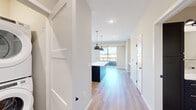 This well-appointed single-floor residence offers a thoughtfully designed layout across two bedrooms, one bathroom, an entrance, and a dedicated closet. Light-toned hardwood-style flooring flows seamlessly throughout the main living areas, complementing the clean, neutral palette of the walls and trim.

The open-concept kitchen and living area serves as the heart of the home. The kitchen is a standout feature, showcasing a striking two-tone design with navy lower cabinets, crisp white upper cabinetry, and light quartz countertops. A large center island with matching navy cabinetry provides generous prep space and is accented by a pair of matte black dome pendant lights suspended from brass fixtures. Stainless steel appliances, a subway tile backsplash, and a matte black faucet complete the contemporary aesthetic. A sliding glass door opens to an outdoor balcony, allowing natural light to pour into the living area.

The primary bedroom is generously sized, featuring large windows with views of the surrounding neighborhood and built-in shelving. The second bedroom offers plush carpeting and a closet with direct natural light from a side window. The bathroom is finished with a dark wood vanity, white quartz countertop, and a full tub-shower combination accented with matte black fixtures.