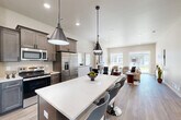 Located at 4411 Dacha Drive in Billings, Montana, this single-story, 3-bedroom, 2-bathroom home offers a thoughtfully designed open-concept floor plan with modern finishes throughout. The heart of the home is the kitchen, which features rich, gray-toned cabinetry, stainless steel appliances, a subway tile backsplash, and a generous central island with a crisp white countertop and bar seating — ideal for casual dining or entertaining. Pendant lighting and recessed ceiling lights illuminate the space, which flows seamlessly into the dining and living areas. The living room is bright and airy, with natural light streaming through large windows and a sliding glass door that provides outdoor views. Light-toned hardwood-style flooring runs throughout the main living areas, adding warmth and continuity. The primary bedroom offers a comfortable, well-proportioned retreat, while the two additional bedrooms feature plush carpeting and large windows. The bathrooms are finished with dark-toned vanities, white countertops, and wood-style flooring. Additional spaces include a pantry, laundry room, utility room, and five closets for ample storage. The attached garage features a concrete floor, an automatic opener, and an interior access door, completing this practical and stylish home.