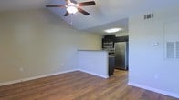 This single-floor space offers a well-designed open-concept layout that seamlessly connects the living area to the kitchen. The living area is finished with warm hardwood flooring that extends throughout, adding a sense of cohesion and warmth to the space. A notable architectural feature is the vaulted ceiling, which lends an airy, expansive feel and is complemented by a ceiling fan that enhances comfort and airflow.

The kitchen is defined by a breakfast bar-style peninsula with a granite-style countertop, providing both a functional workspace and a casual dining or entertaining surface. Dark cabinetry lines the kitchen walls, creating a striking contrast against the stainless steel appliances, which include a refrigerator, microwave, and range. The kitchen is well-lit with overhead lighting, ensuring a bright and practical workspace.

The neutral, light-toned walls throughout the space provide a clean and versatile backdrop that accommodates a variety of interior design preferences. White baseboards add a crisp finishing detail. Overall, the space presents a functional and modern aesthetic, combining practical design with comfortable living features suited to everyday use.