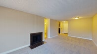 Located at 8330 E Quincy Ave in Denver, Colorado, this single-floor residence offers a well-organized layout with a range of functional living spaces. The main living area is anchored by a classic tile-surround fireplace set against neutral-toned walls, with plush carpeting underfoot and a textured ceiling overhead. Built-in shelving is visible in the background, adding practical storage to the space. An adjacent area features a sliding glass door that opens to a private balcony, allowing natural light to fill the room and offering views of surrounding greenery. The bedroom continues the carpeted flooring and includes direct access to both a closet and a full bathroom, with a second sliding glass door providing additional balcony access and outdoor views. The kitchen is outfitted with warm wood cabinetry, granite-style countertops, a stainless steel sink, a dishwasher, and a refrigerator, all complemented by light hardwood-style flooring. The bathroom features a clean, fully tiled tub and shower surround in crisp white. Throughout the space, baseboard heating ensures year-round comfort, and the neutral color palette creates a cohesive, move-in-ready environment.